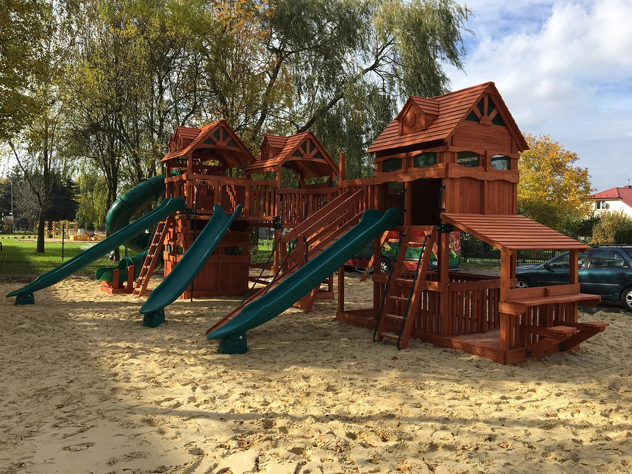 Wooden playground structure with slides and sand area in a park setting