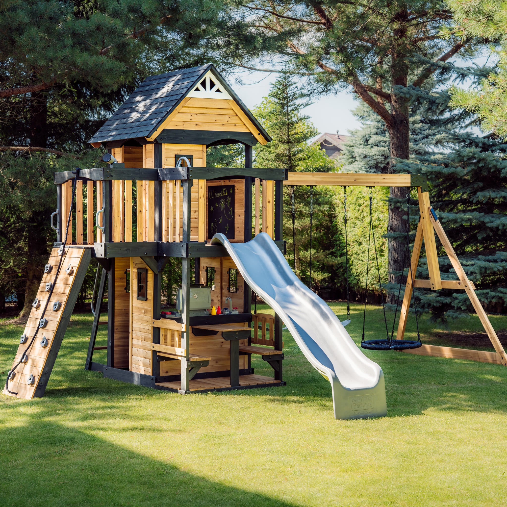 Canyon Creek cedar swing set from the front left showing the climbing ramp, lower playhouse kitchen and web swing