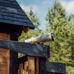 Telescope mounted on the upper fort of the Canyon Creek cedar swing set against pine trees